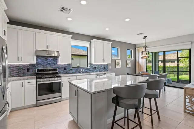 a kitchen with stainless steel appliances granite countertop a stove a sink dishwasher a microwave oven and a dining table with wooden floor