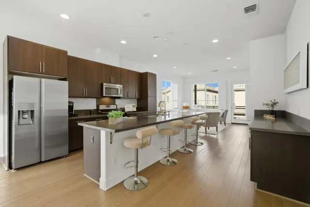 a kitchen with stainless steel appliances kitchen island granite countertop a refrigerator a stove a sink a oven and white cabinets with wooden floor