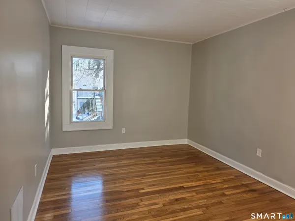 a view of an empty room with wooden floor and a window