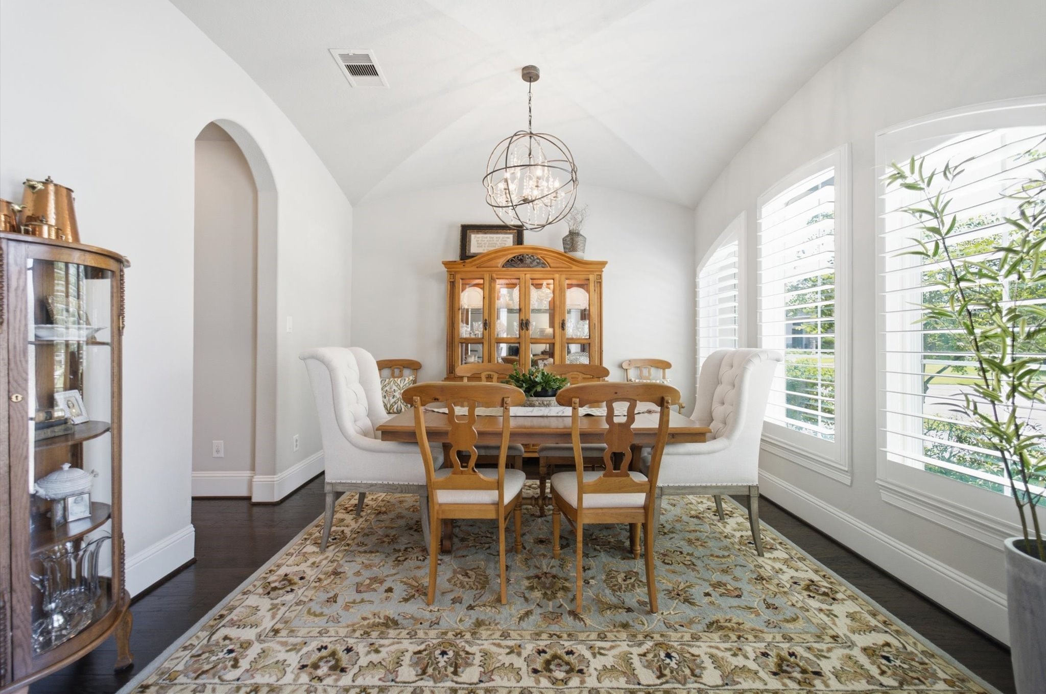 23722 Thortons Park Lane Spring, TX 77389 - Photo 8 of 48 This elegant dining room features a vaulted ceiling, large windows with shutters for natural light, and a stylish chandelier. It includes a wooden dining table with upholstered chairs and a charming display cabinet, set on a decorative rug.