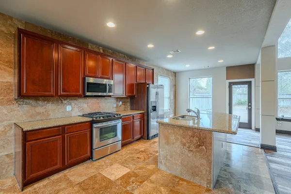 a kitchen with stainless steel appliances granite countertop a refrigerator a stove and a sink with wooden cabinets