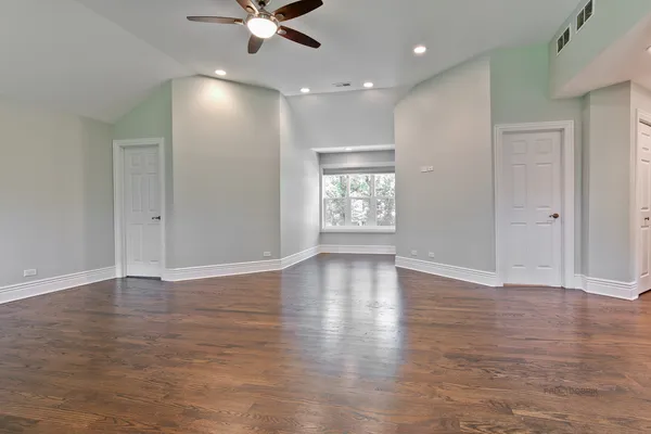 an empty room with wooden floor fan and windows
