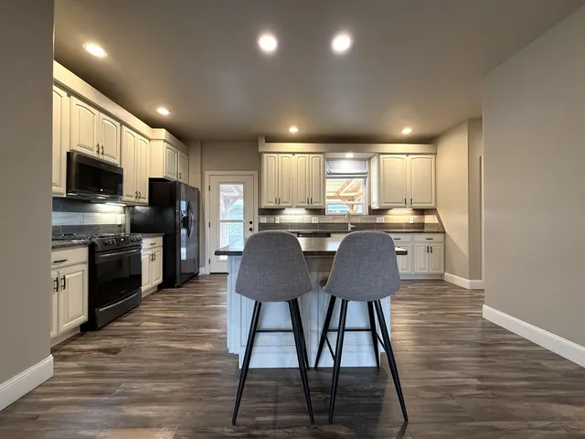 a large kitchen with kitchen island granite countertop a stove top oven a sink and white cabinets