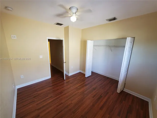 a view of an empty room with wooden floor and a ceiling fan