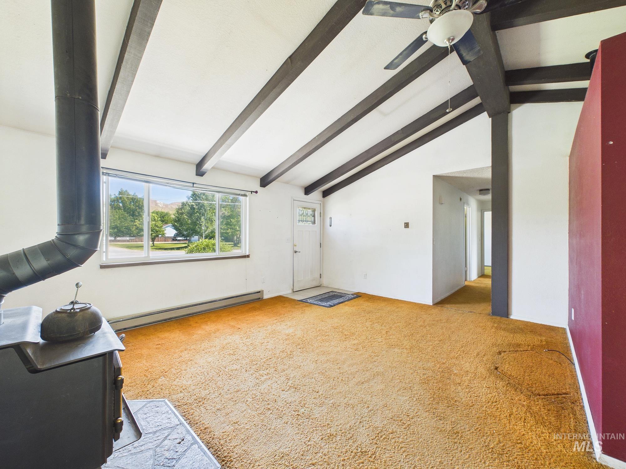 1527 North Plaza Road Emmett, ID 83617 - Photo 8 of 33 Living space featuring exposed ceiling beams, a wood-burning stove with a hearth, and a front-facing window
