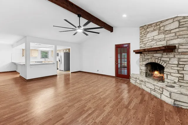 an empty room with wooden floor chandelier fan and windows