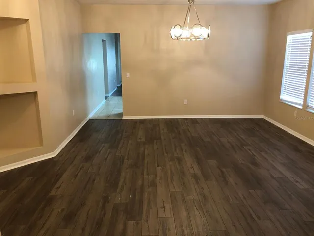 an empty room with wooden floor chandelier and windows