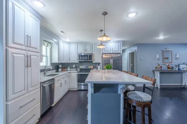 a kitchen with stainless steel appliances kitchen island granite countertop a sink dishwasher a stove and white cabinets with wooden floor