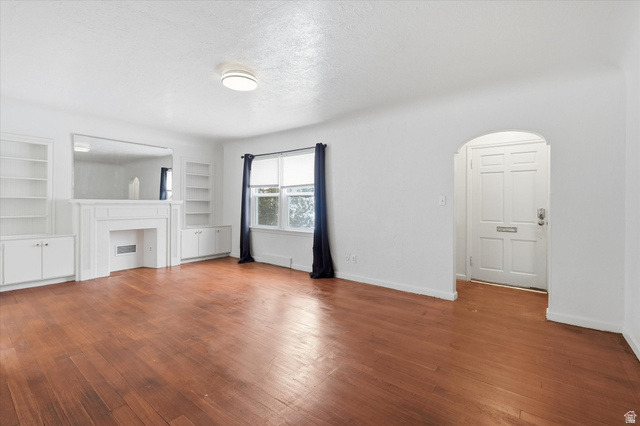 744 North 500 East Logan, UT 84321 - Photo 4 of 29 Unfurnished living room with arched walkways, hardwood / wood-style flooring, a textured ceiling, built in features, and a fireplace