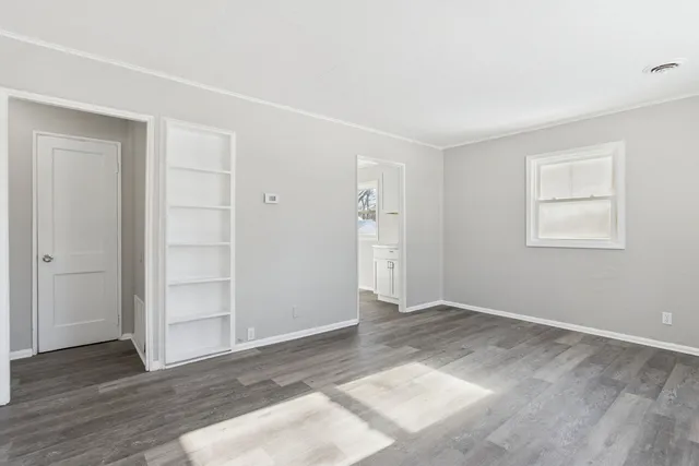 an empty room with wooden floor closet and windows