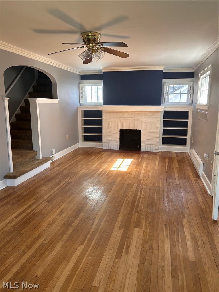 1001 Englewood Road Cleveland Heights, OH 44121 - Photo 9 of 28 Unfurnished living room with crown molding, hardwood / wood-style floors, ceiling fan, a brick fireplace, and baseboard heating