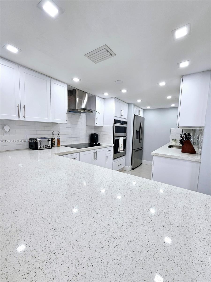 a large white kitchen with kitchen island a sink a stove a refrigerator and white cabinets with wooden floor