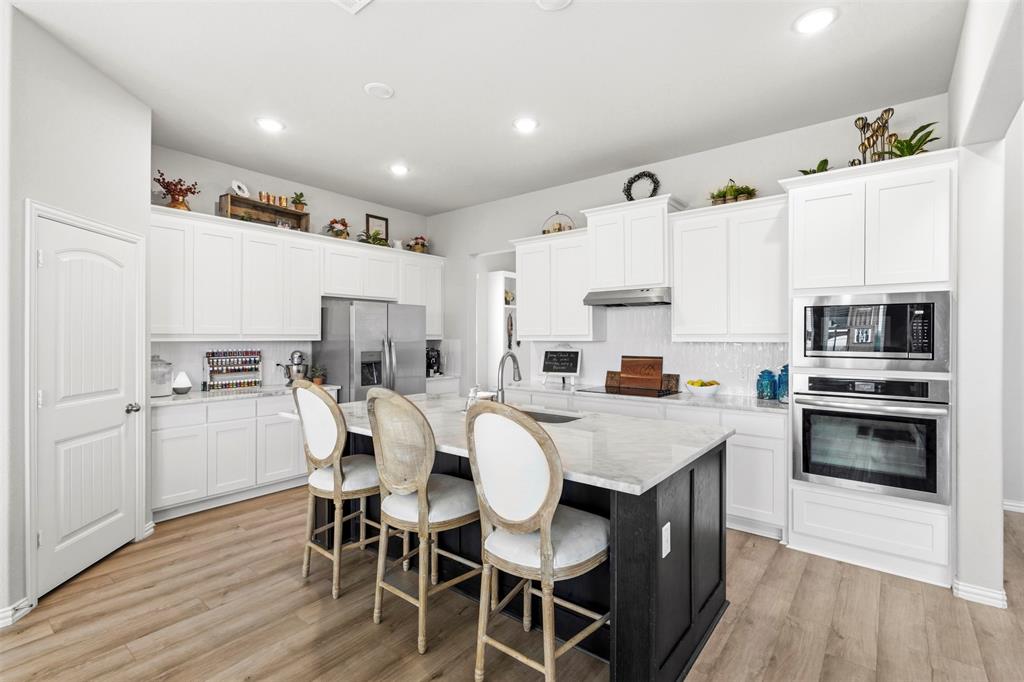 107 Yampa Court Rhome, TX 76078 - Photo 13 of 30 Spacious kitchen featuring an expansive island with seating, extensive white cabinetry, stainless steel appliances, wood-finish flooring, and recessed lighting