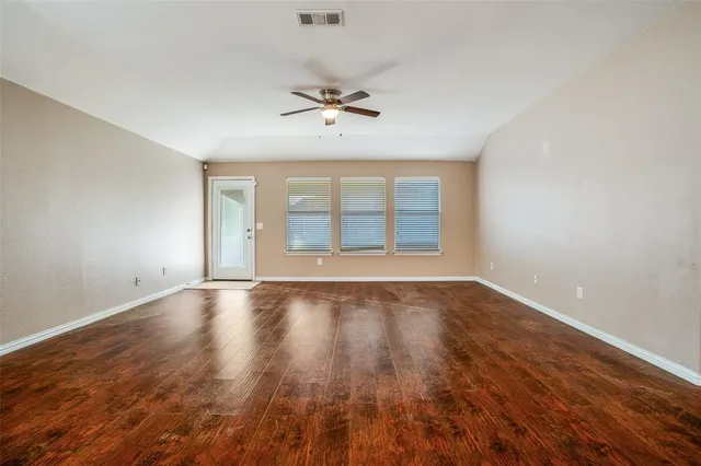 an empty room with wooden floor ceiling fan and windows