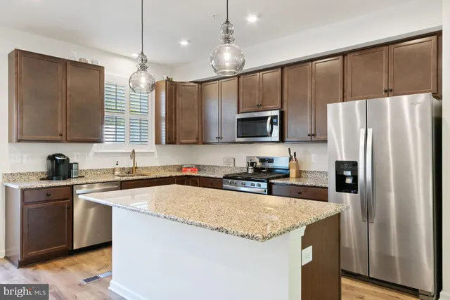 a kitchen with stainless steel appliances granite countertop a refrigerator a sink dishwasher a stove top oven a kitchen island and couches with wooden floor