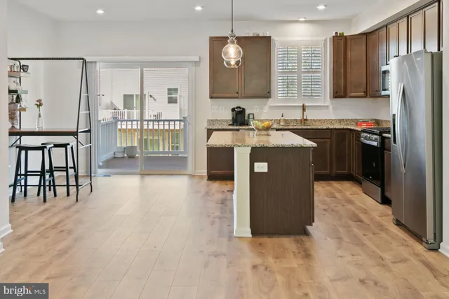 a kitchen with stainless steel appliances granite countertop a stove top oven a refrigerator a sink and a dining table with wooden floor