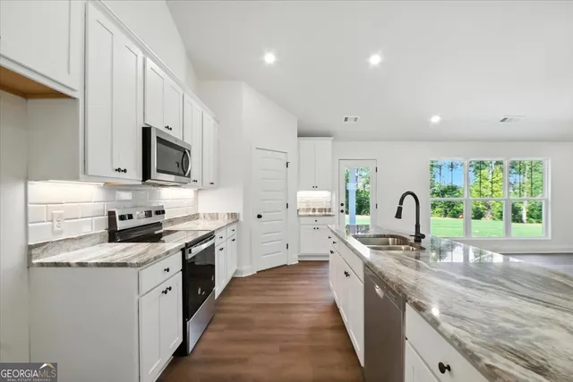 a kitchen with stainless steel appliances granite countertop a sink a stove a refrigerator cabinets and a wooden floor