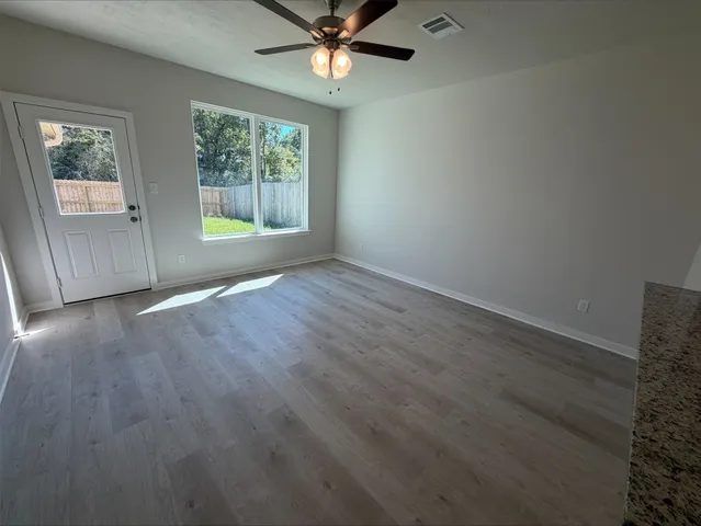 an empty room with wooden floor chandelier fan and windows