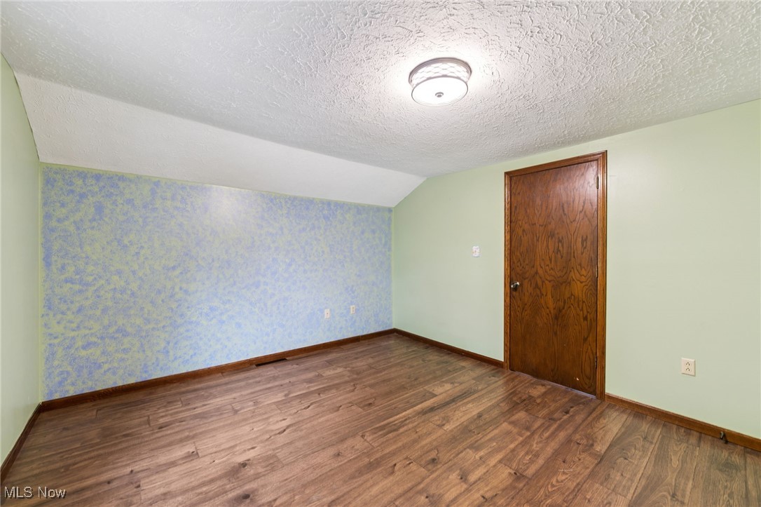 12422 Portage Street Rittman, OH 44270 - Photo 21 of 42 Additional living space with dark wood-style flooring, a textured ceiling, vaulted ceiling, and wallpapered walls