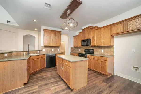 a kitchen with stainless steel appliances granite countertop a stove top oven a sink dishwasher and a refrigerator with wooden floor