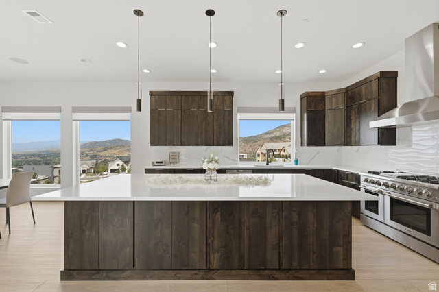 1445 Jacob Road Sandy, UT 84092 - Photo 10 of 52 Spacious kitchen featuring an expansive central island with a white solid surface countertop, dark wood-finish cabinetry, a large stainless steel range with a professional-grade hood, and multiple windows showcasing a mountainous landscape