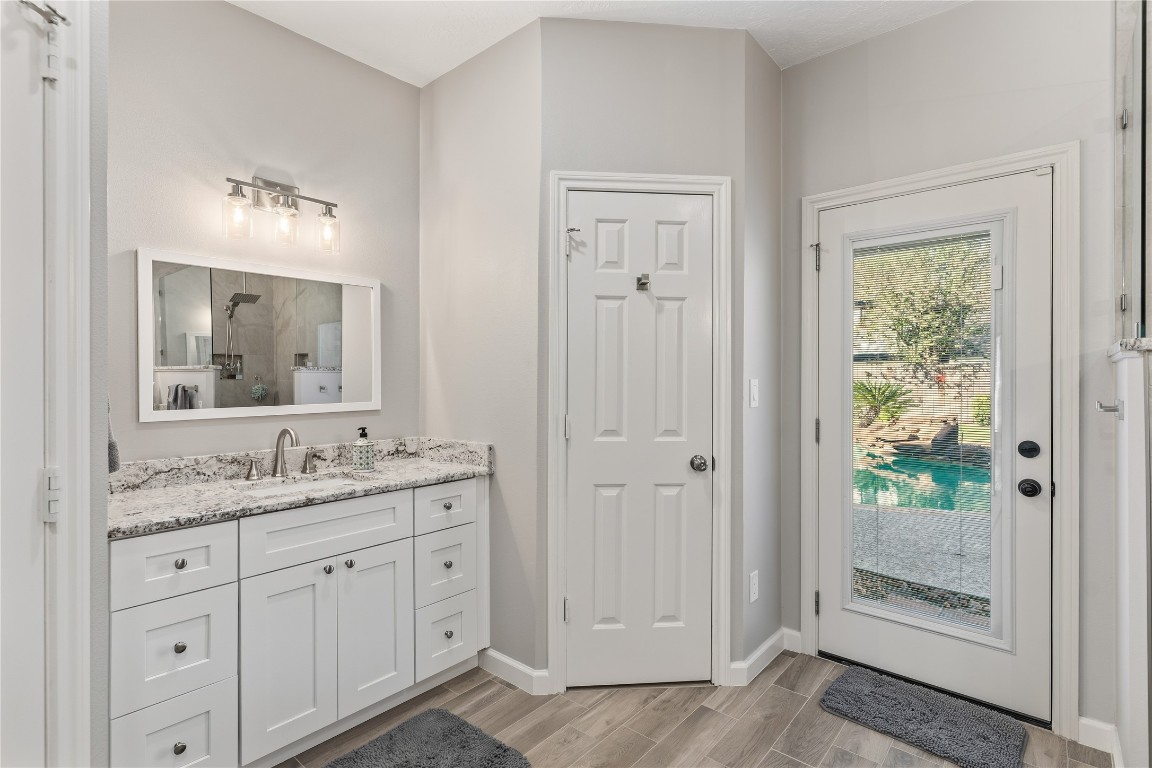 6618 Wimbledon Trail Road Spring, TX 77379 - Photo 23 of 43 The primary bathroom features a granite countertop with dual vanities, large mirrors, and stylish lighting. A glass door opens to a view of a backyard pool, enhancing the space with natural light and a serene outlook.