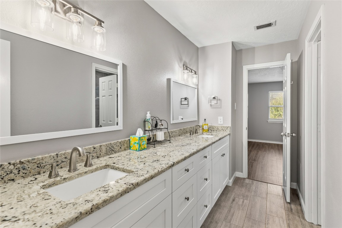 6618 Wimbledon Trail Road Spring, TX 77379 - Photo 28 of 43 This bathroom features a modern design with dual sinks, granite countertops, and stylish lighting fixtures. It has a neutral color palette and connects to a room with wood-look flooring, enhancing the home's cohesive and contemporary feel.