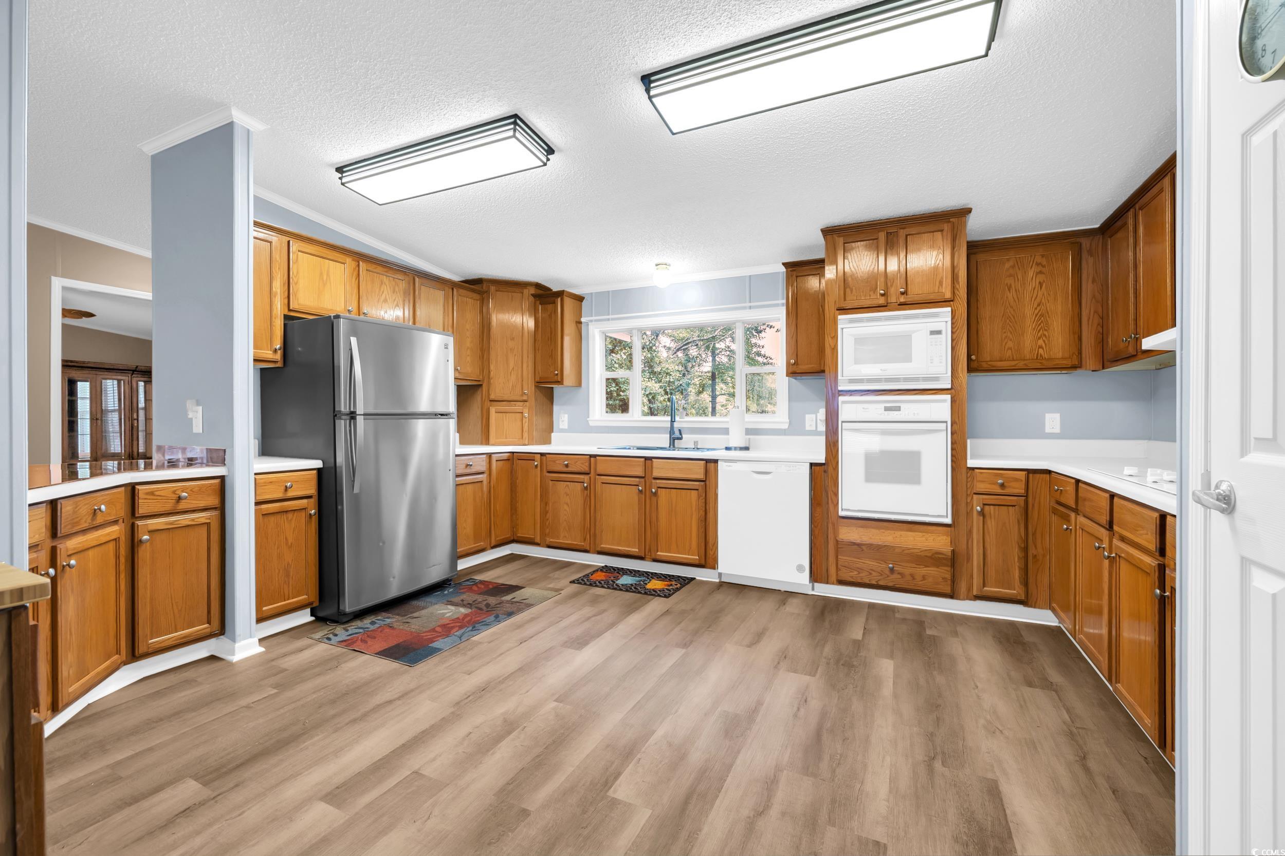3373 Lake Pond Road Loris, SC 29569 - Photo 13 of 33 Kitchen featuring brown cabinetry, white appliances, ornamental molding, light countertops, and a textured ceiling