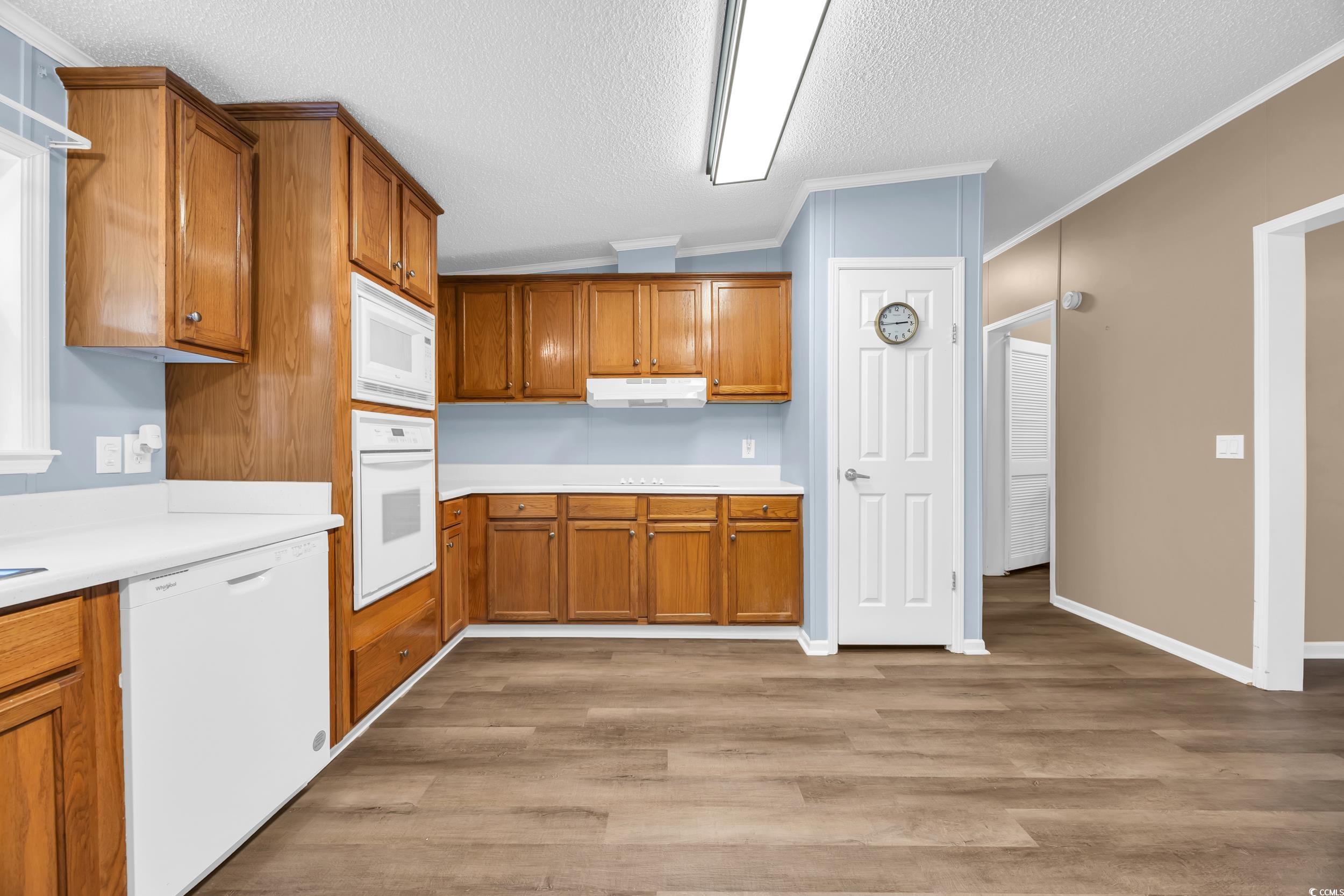 3373 Lake Pond Road Loris, SC 29569 - Photo 14 of 33 Kitchen featuring brown cabinets, ornamental molding, white appliances, light wood finished floors, and light countertops