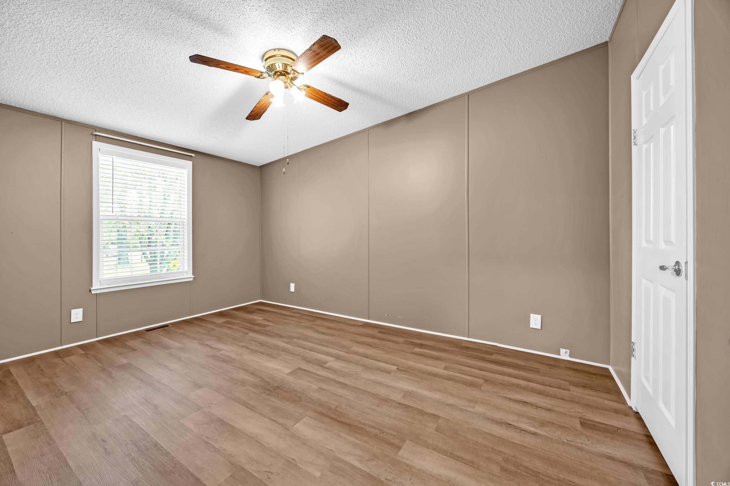 3373 Lake Pond Road Loris, SC 29569 - Photo 19 of 33 Empty room with a ceiling fan, a textured ceiling, wood finished floors, and a decorative wall
