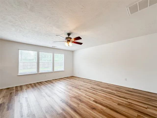 an empty room with wooden floor fan and windows