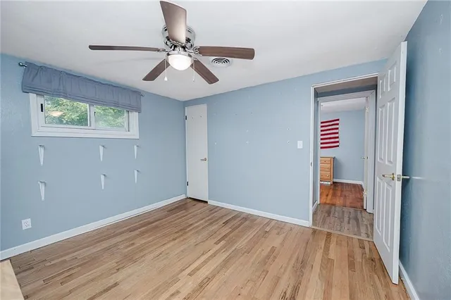 a view of an empty room with wooden floor and a ceiling fan