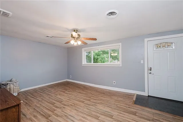 an empty room with wooden floor chandelier fan and windows
