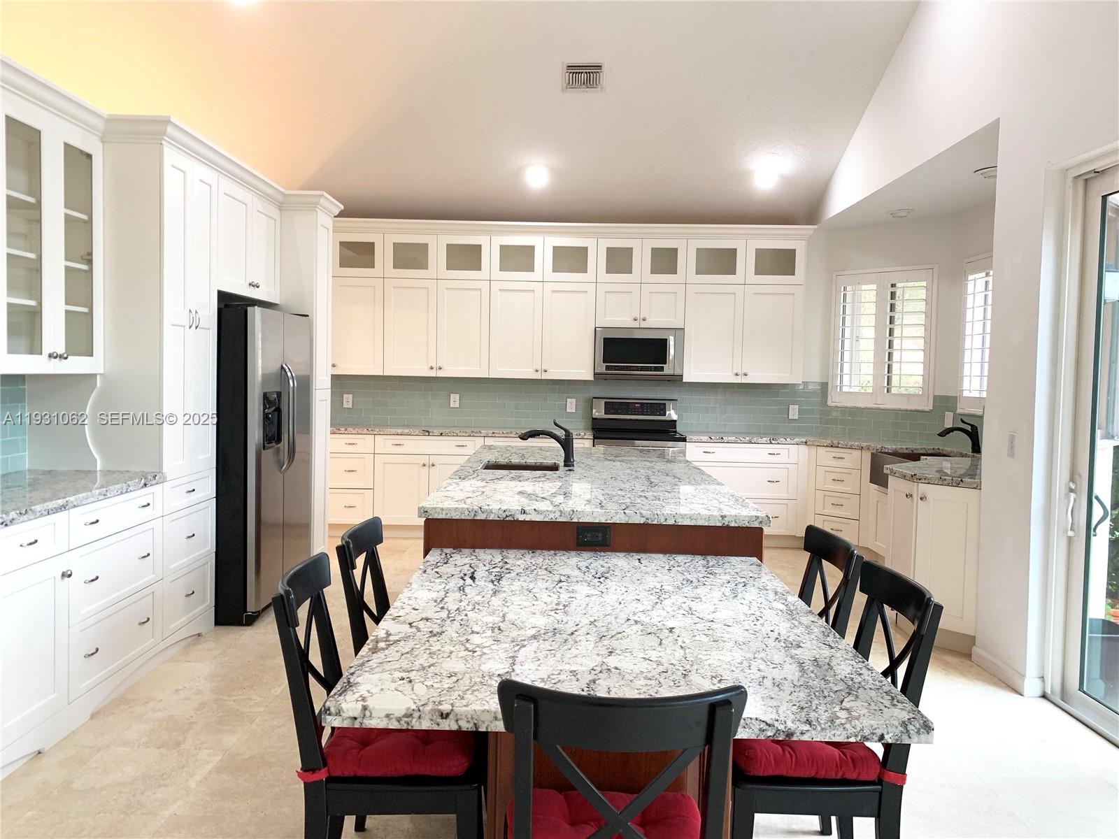 a kitchen with stainless steel appliances kitchen island granite countertop a dining table chairs and a refrigerator