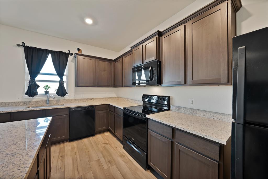 233 Lewis Lane Venus, TX 76084 - Photo 9 of 40 Another angle of the kitchen showcasing island seating, stainless-style appliances, and open flow to the living area.