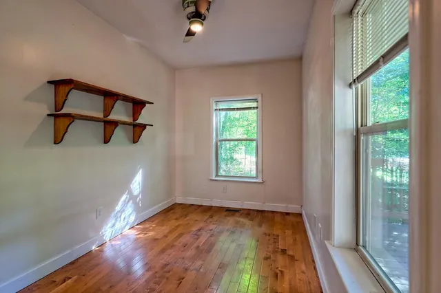 an empty room with wooden floor fan and a window