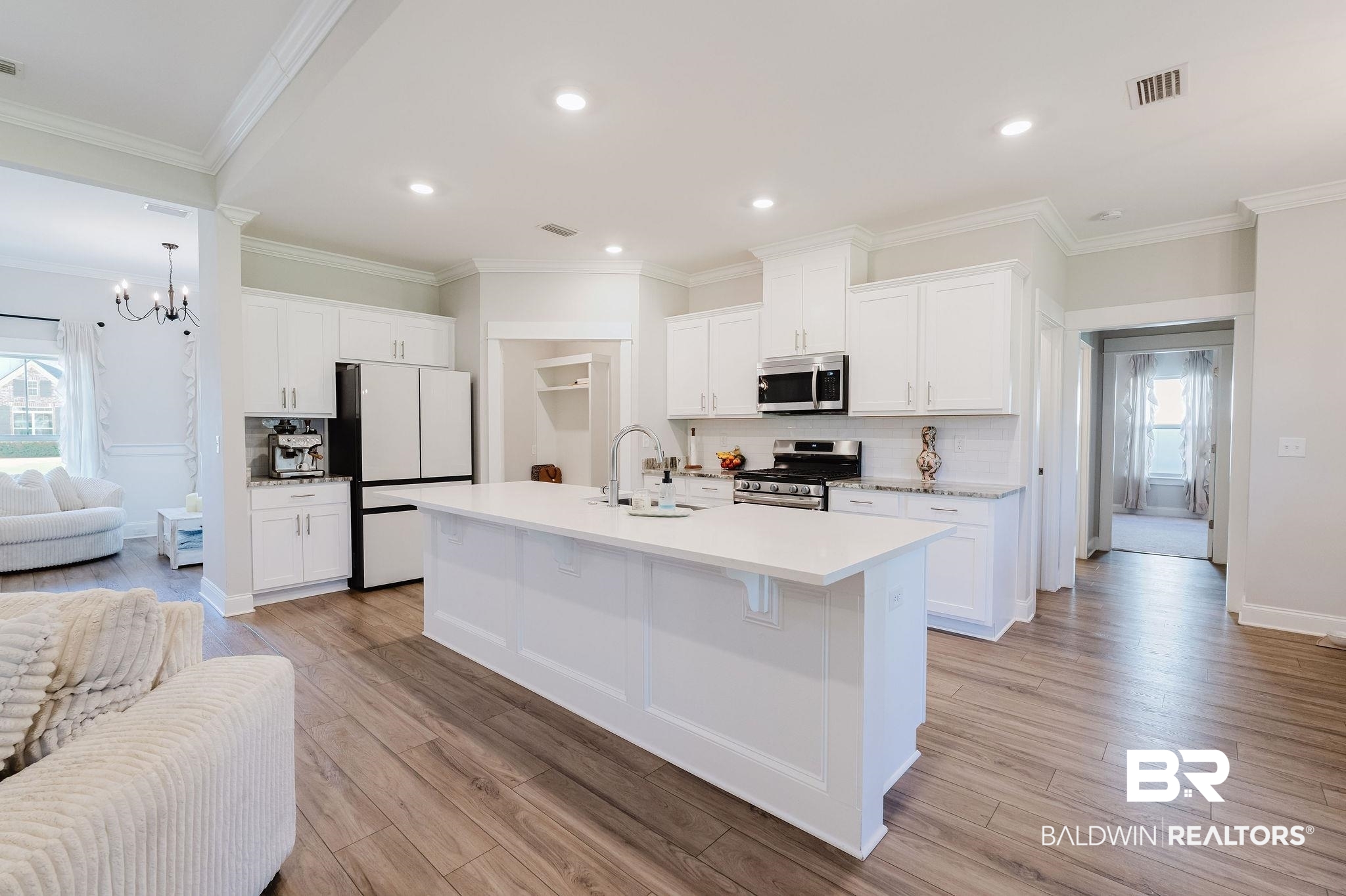 7872 Calverton Street Foley, AL 36535 - Photo 34 of 76 Bright kitchen featuring a large central island, white cabinetry, integrated stainless steel appliances, light-toned countertops, and wood-finish flooring