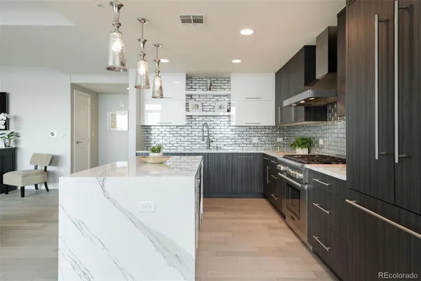 a large kitchen with stainless steel appliances kitchen island granite countertop a large kitchen island a stove a refrigerator a sink dishwasher and white cabinets with wooden floor