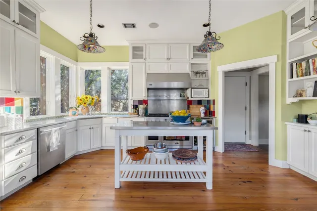 a open kitchen with stainless steel appliances granite countertop a stove a sink dishwasher a dining table and chairs with wooden floor