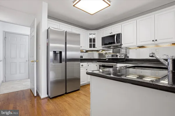 a kitchen with stainless steel appliances granite countertop a sink a microwave a refrigerator and white cabinets
