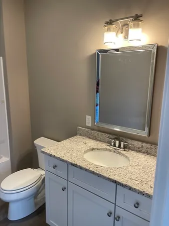 a bathroom with a granite countertop toilet sink and mirror