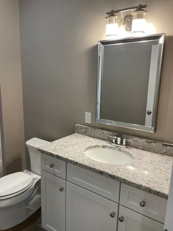 a bathroom with a granite countertop sink a toilet and mirror