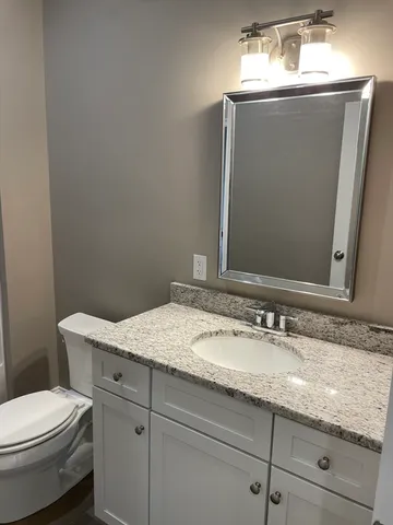 a bathroom with a granite countertop sink a toilet and mirror