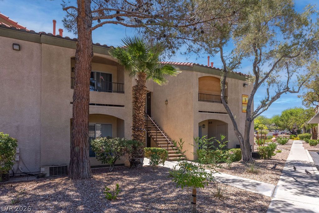 7885 West Flamingo Road, Unit 1016 Las Vegas, NV 89147 - Photo 22 of 24 A Mediterranean-inspired building showcases balconies and exterior stairs amidst mature trees.
