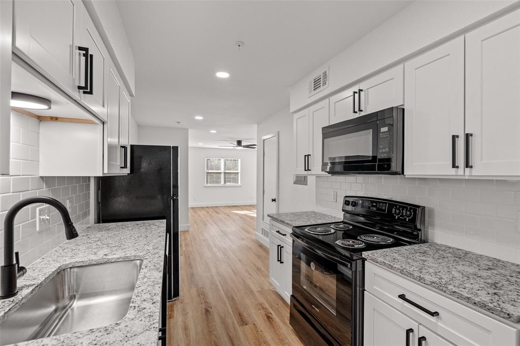 125 13th Street Southeast, Unit 201 Paris, TX 75460 - Photo 4 of 11 a kitchen with stainless steel appliances granite countertop a stove top oven a sink dishwasher a refrigerator with wooden cabinets and floor