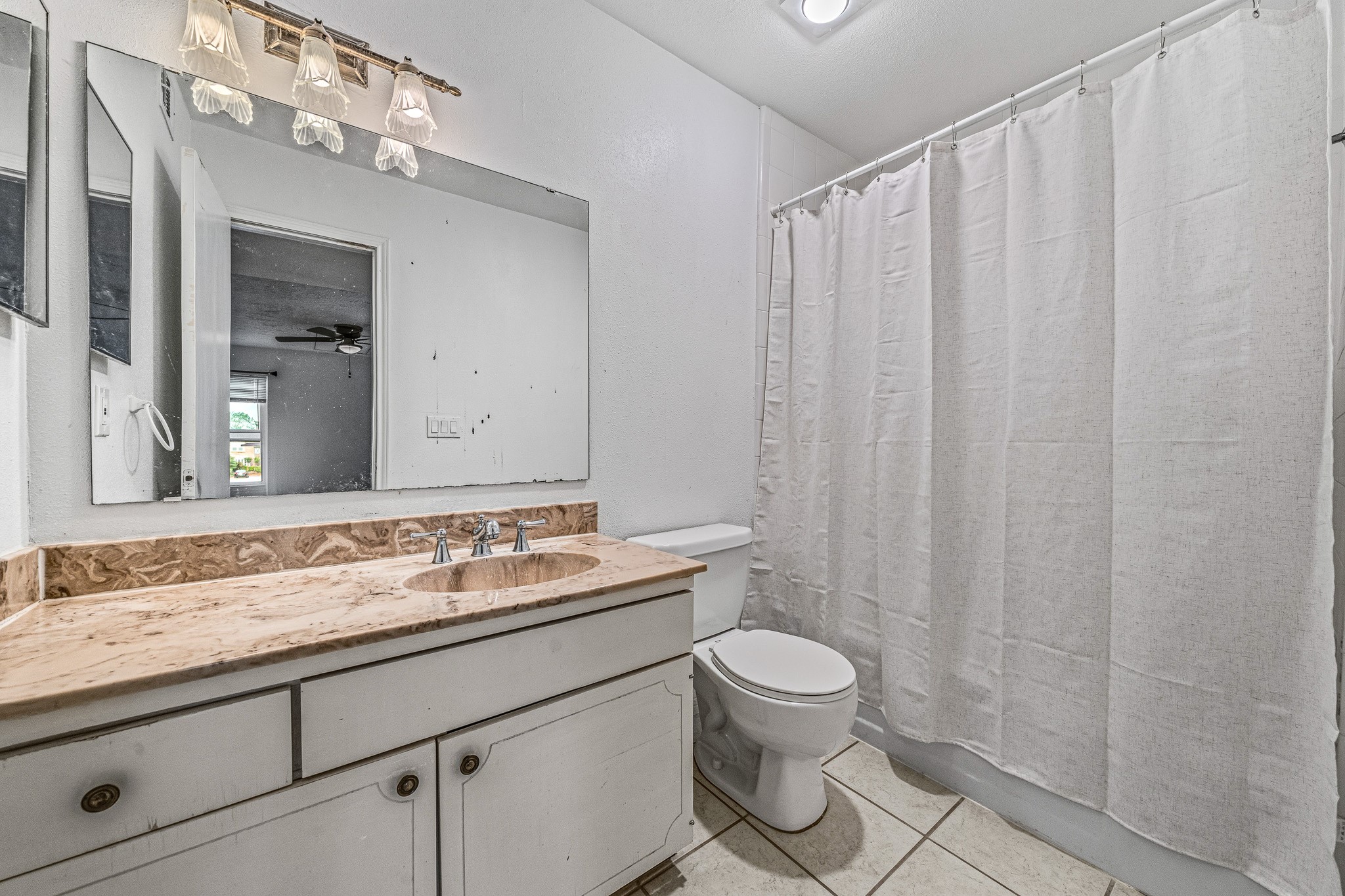 830 Threadneedle Street, Unit 240 Houston, TX 77079 - Photo 21 of 33 This bathroom features a large mirror, marble countertop with a single sink, and a bathtub with a shower curtain. The neutral tones and tile flooring create a clean, simple aesthetic.