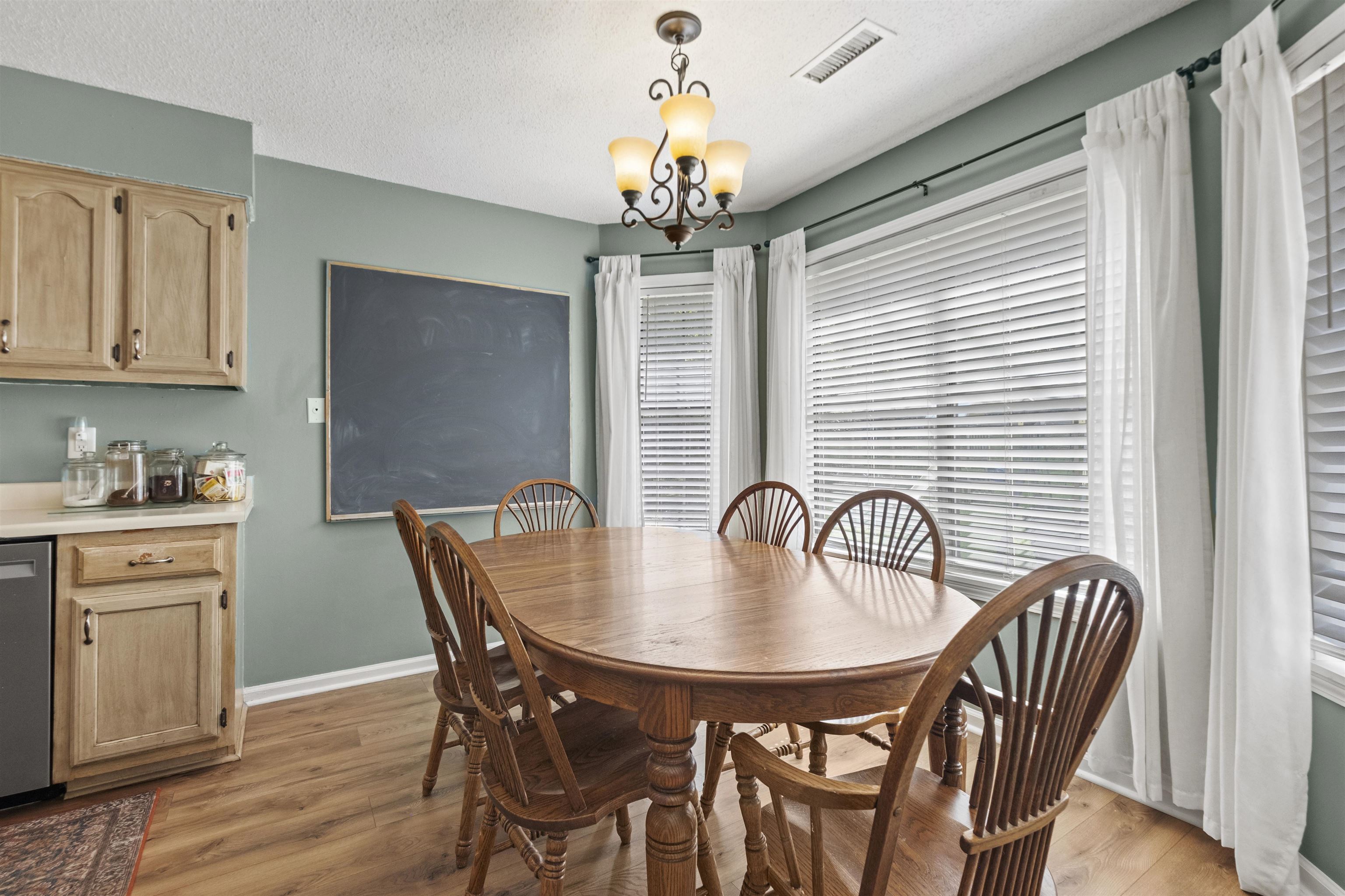 3601 Marshall Road Munford, TN 38058 - Photo 23 of 35 Dining area featuring wood-finish flooring, a multi-window bay with blinds, light green wall paint, and a classic chandelier