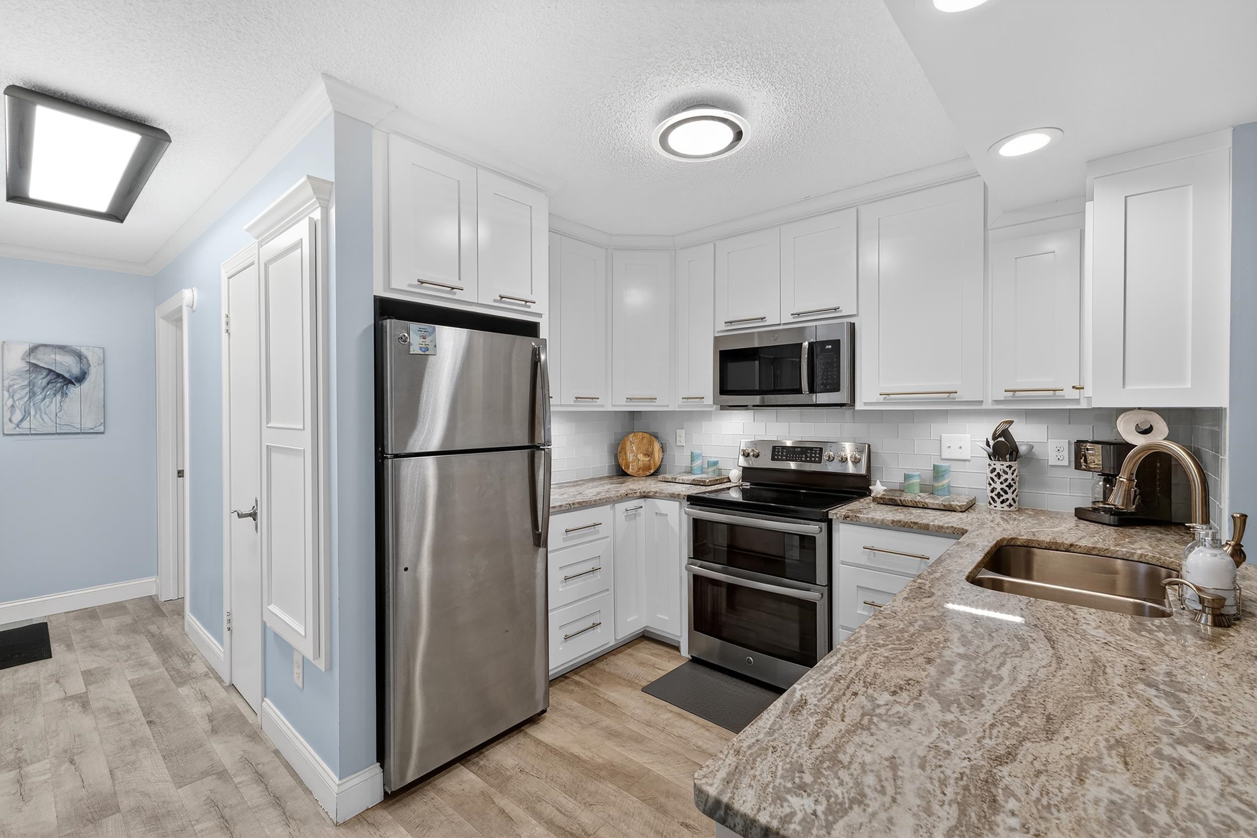 9581 Shore Drive, Unit 229 Myrtle Beach, SC 29572 - Photo 13 of 39 Kitchen with light stone counters, stainless steel appliances, white cabinetry, light wood-style floors, and a textured ceiling