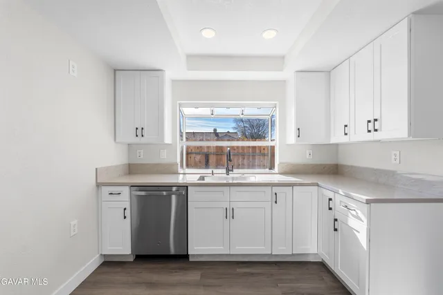 a kitchen with white cabinets appliances a sink and a window