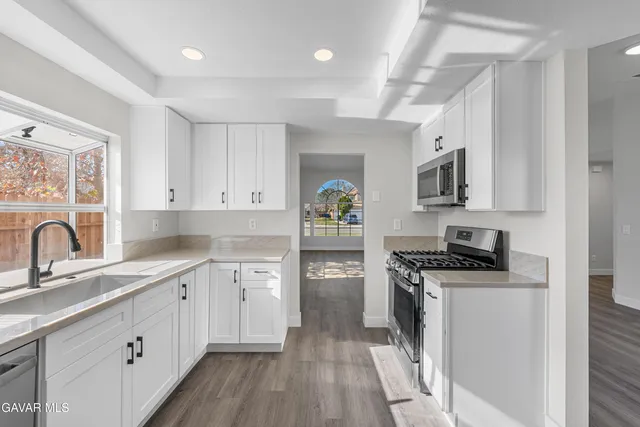 a kitchen with stainless steel appliances a sink dishwasher stove refrigerator and cabinets with wooden floor